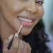 smiling black woman applying lipstick with applicator