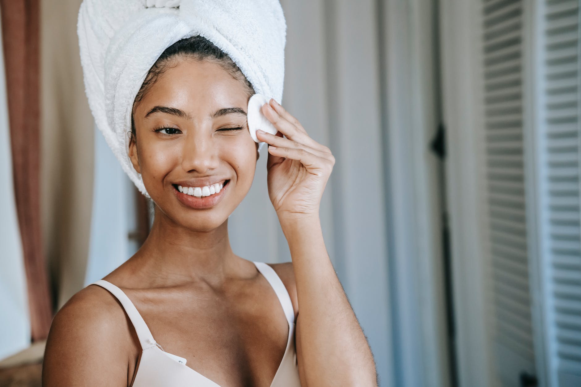 smiling ethnic woman wiping face skin in morning